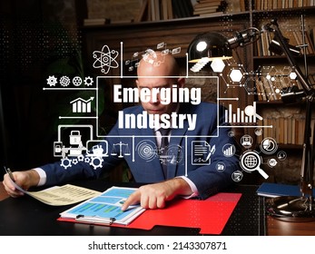 Financial Concept About Emerging Industry With Inscription. Young Finance Market Analyst In Eyeglasses Working While Sitting At Wooden Table On Background.
