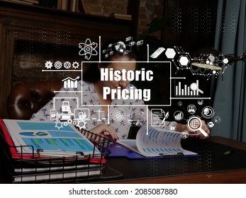 Financial Concept About Historic Pricing With Inscription. Young Finance Market Analyst In Eyeglasses Working While Sitting At Wooden Table On Background.
