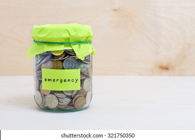 Financial concept. Coins in glass money jar with emergency label. Wooden background