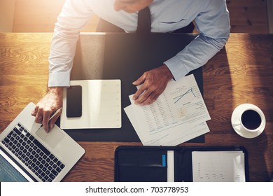 Financial Consultant Sitting At His Desk In An Office Reviewing Documents And Working Online With A Laptop