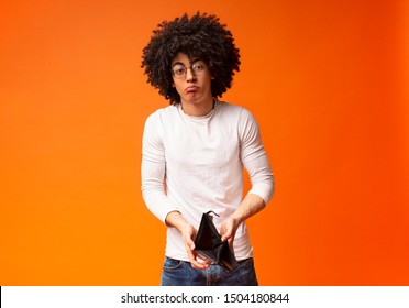 Financial crisis and bankruptcy. Unhappy black guy showing empty wallet, orange studio background