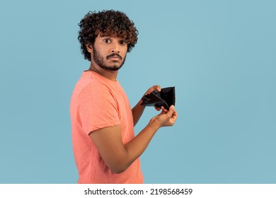 Financial crisis and bankruptcy while COVID-19 pandemic concept. Sad eastern man showing empty wallet at camera, short of money, spent money, blue studio background, copy space - Shutterstock ID 2198568459