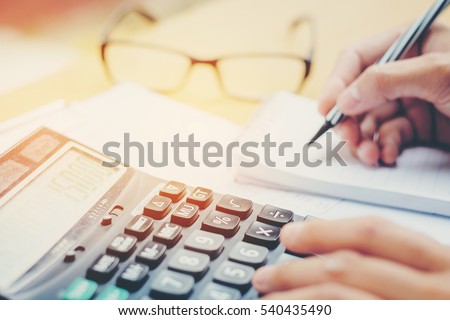 Financial data analyzing hand writing and counting on calculator in office on wood desk