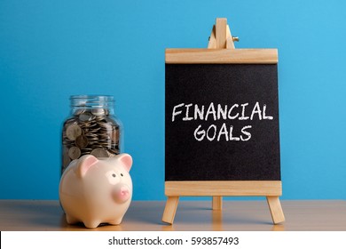 Financial Goals, Financial Concept. Mason Jar With Coins Inside, Piggy Bank And Chalkboard On Wooden Table.