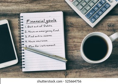 Financial goals on notepad on blank notepad with calculator, coffee, pen and smart phone on a wooden table, retro style. - Powered by Shutterstock