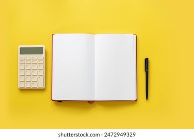 Financial objects - calculator and blank open page book on yellow background still life. Overhead view.