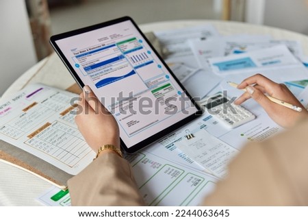 Financial paperwork. Unrecognizable person performs arithmetic operations calculates costs per month controls expenses surrounded by papers and bills manages household budget. Close up cropped view