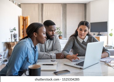 Financial planner going over savings plans on a laptop with a young African American couple at a table in their living room at home