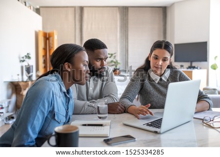 Financial planner going over savings plans on a laptop with a young African American couple at a table in their living room at home