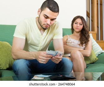 Financial problems in family. Man counting money, woman watching him in living room 