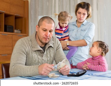 Financial Problems In Family. Sad Woman Wit Children Against Husband At Home With Money