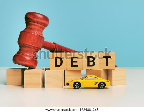 Financial and\
property concept. Phrase DEBT on wooden cubes with gavel and\
miniature car isolated on blue\
background.