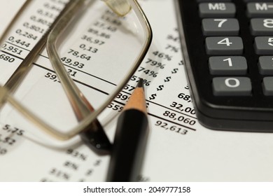 Financial report, calculator, pencil and glasses on the table in the office. A paper sheet full of business data. Accounts number on the data paper. Business documents on office table. Closeup.