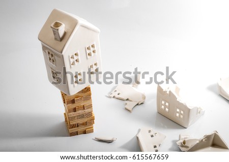 Financial risk, unstable real estate investment and shaky housing market concept with a home on stacked wooden building blocks surrounded by the ruins and debris of another house that collapsed