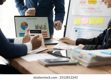 Financial Synergy in Action: A team huddles around a desk, collaborating on data analysis with calculators and laptops, as a presenter highlights key figures on a whiteboard.  - Powered by Shutterstock