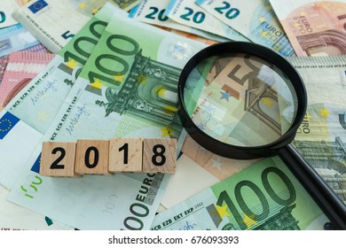 financial tax concept as magnifying glass on pile of euro banknotes and number 2018 on wooden block.
