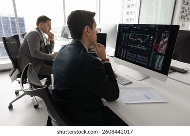 Financial trader man analyzing stock market, thinking on investment strategy, touching chin, looking at analytic data, growth chart on monitor, working on foreign exchange platform