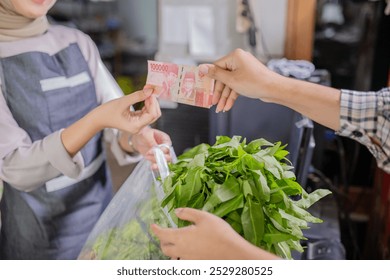 A financial transaction is happening in a busy market where a consumer is buying fresh greens - Powered by Shutterstock