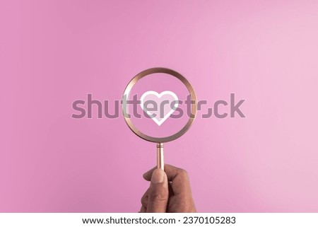 find love concept for Valentine day,marriage and romantic moment.red heart icon and hand holding the magnifier glass on pink background.