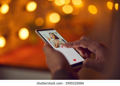 Find love online concept. Man holding mobile phone, looking at attractive young woman's profile photo on dating app and pressing red heart like button. Close-up, blur, romantic bokeh, soft focus