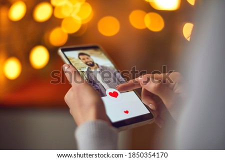 Find love online concept. Woman looking at attractive young man's profile photo on dating app and pressing red heart like button. Close-up of female hands holding mobile phone. Blur, bokeh, soft focus