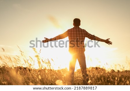Finding inner happiness. Young man in open country field with his arms outstretched facing the beautiful warm sunrise.  Mind body and spirit concept. 