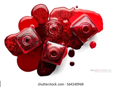 Fine art cosmetics and beauty image. Nail art concept with a set of trendy red nail polish spilled around four opened bottles viewed top down, different shades and metallic lustre isolated on white