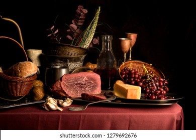 Fine art food image reminiscent of 17th Century still life painting featuring meat, cheese, grapes, bread and garlic. Shot with various props relevant to that era and lit with moody studio flash. 