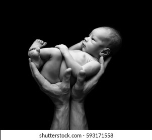 Fine Art Image Of A Father's Hands Holding His Baby Against A Black Background