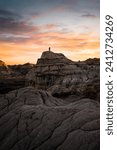 A fine art landscape photography image of Dinosaur Provincial Park with a solo adventurer standing atop a prominent badlands pillar during a dynamic and vibrant sunset