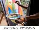 Fine arts african young student holding a palette with paint while painting a picture of a colorful lion