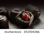 fine chocolate pralines with red fruit filling on a dark rustic wooden background, macro shot with selected focus and narrow depth of field