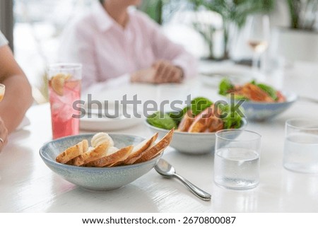 Fine dining table setting with elegant food presentation, featuring fresh salad, prawns, crusty bread, and colorful drinks in soft daylight