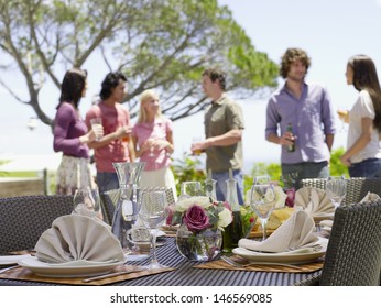 Fine Dining Table Setting With Friends Enjoying Drinks In Background