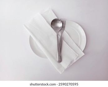 The fine dining table setting is placed in a white classic style, with a tissue napkin, a silver spoon, and a fork. Flat lay or top view. Isolated on a white background.