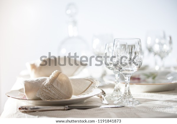 Fine dinning: floral pattern white china dinner\
set arranged on a table with vintage tablecloth and napikins,\
crystal glassware. Selective\
focus.