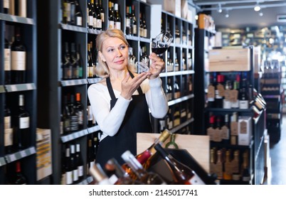 Fine mature female vintner proposing degustation of wine in modern wine shop - Powered by Shutterstock