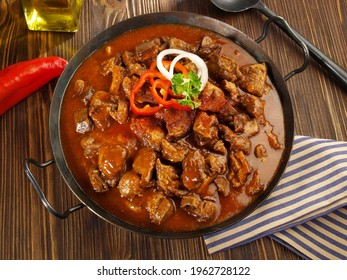 Fine Meat - Beef Goulash in a Pan with Red Pepper on wooden Background.