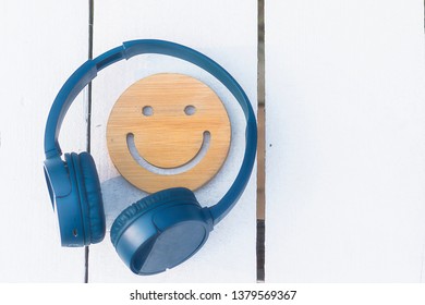 Fine Music For Perfect Mood. Wireless Headphones Of Blue Color And A Wooden Smile Lie On A White Background. No People. Modern Technology. Copyspace