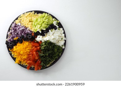 Finely chopped vegetables, orzo pasta, mozzarella cheese, basil and olives lie on a large plate. Ingredients for preparing a Mediterranean salad with orzo pasta.