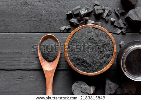 Finely ground charcoal in a cup rests on an old black wooden table.