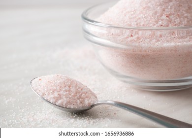 Finely ground Pink Himalayan Salt in a metal spoon in front of a glass bowl full of salt on a white kitchen worktop. - Powered by Shutterstock