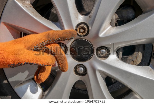 Finger of hand with orange gloves pointing at car
wheel bolt
