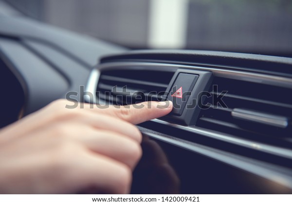 Finger hitting\
emergency light stop botton in the car , man pressing red triangle\
car hazard warning\
button.