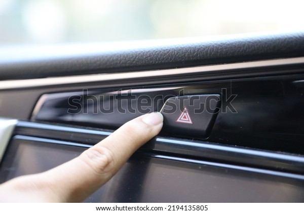 Finger hitting emergency light stop botton in the\
car , man pressing red triangle car hazard warning button. car\
emergency button