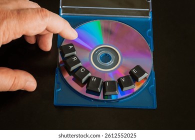 A finger hovering over a computer compact disc labeled "archive" made from computer keyboard keys, on a dark background, close-up shot, technology from the 20th century