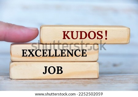 Finger pointing KUDOS text on wooden blocks with wooden cover background. Achievement concept.