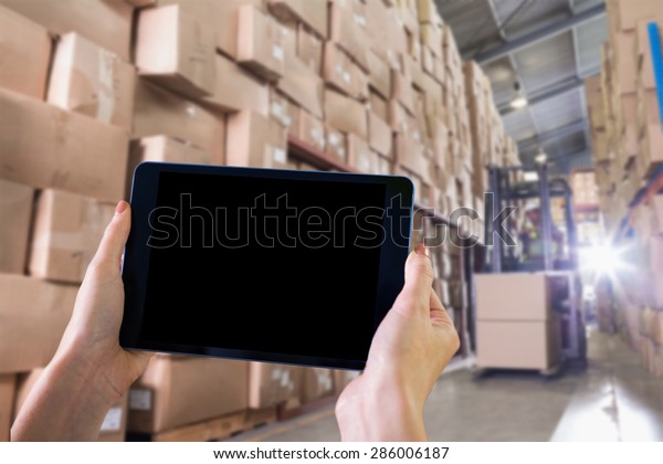 Finger pointing to tablet against forklift\
machine in warehouse