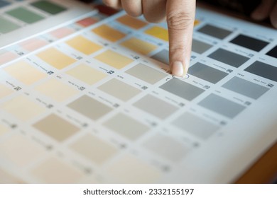 a finger points to the medium dark gray color box on the paint color catalog, no people