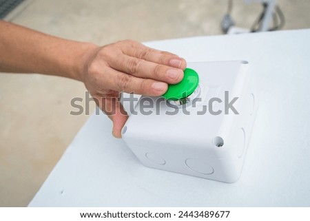 Finger press button of control switch on board with white background and green button to open or start operate .